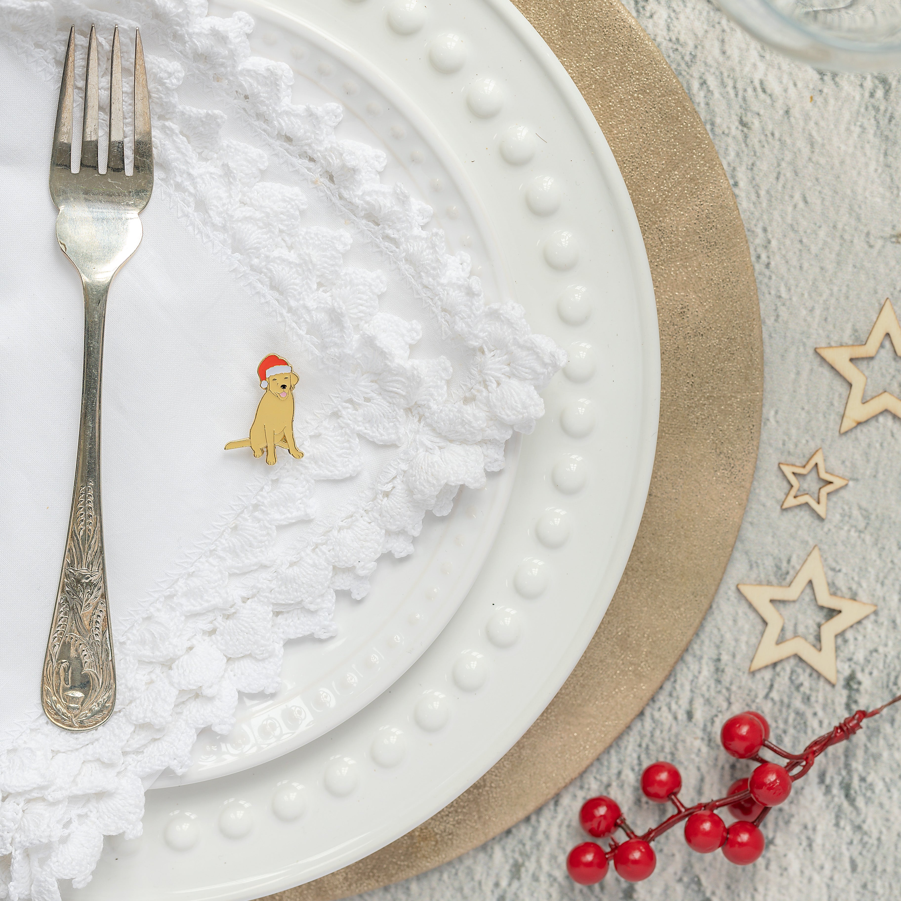Christmas table setting with golden Labrador pin badge on top of a white napkin next to a fork