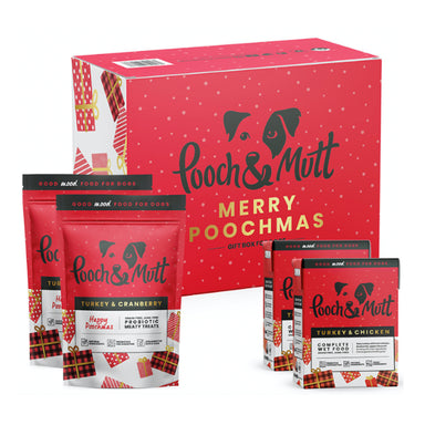 A red gift box with the Pooch & Mutt logo and the text 'Merry Poochmas' in gold. Two pouches of meaty treats and two cartons of wet food are shown next to the box.
