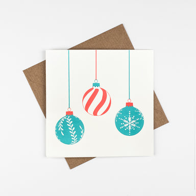 A trio of hanging baubles on a white background. The left bauble is a turquoise blue with a white wreath style design, the middle bauble is red and white swirl stripes and the right bauble in a turquoise blue.