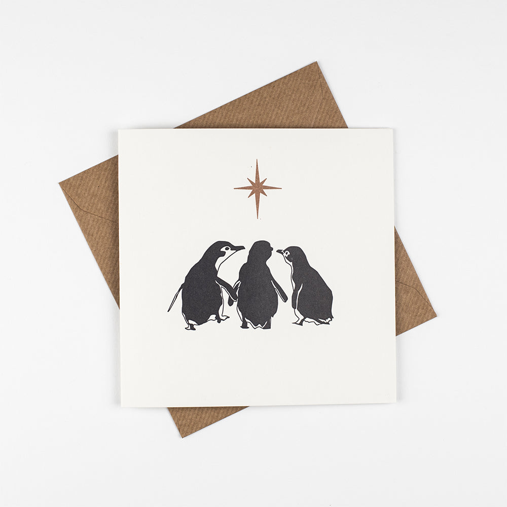 The design is the back of three silhouetted penguins looking towards a golden star on a white background. 