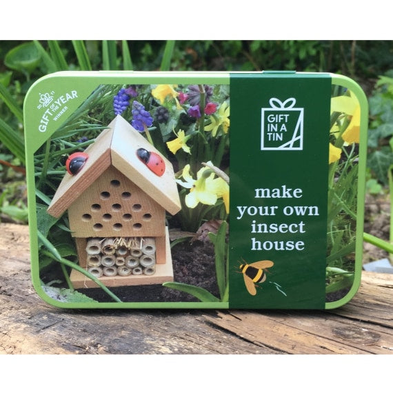 A green tin with a picture on the lid of a wooden insect house in a garden.