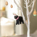 A black wool felt Labrador decoration with pink and white ears, and a pink collar hanging on an Easter tree.