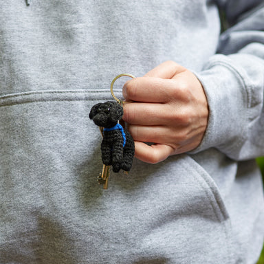 A black crocheted labrador keyring being held in a person's hand.