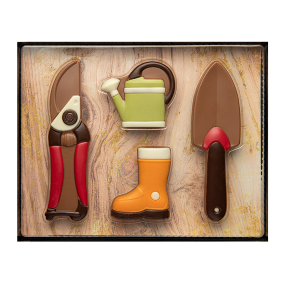 A pair of pliers, an orange welly boot, a green watering can, and a trowel all made out of solid chocolate on a wood effect background.