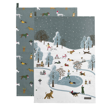 Two tea towels, one with an overall pattern of dogs in Christmas hats and scarves, the other with a scene of a park in winter with people skating, skiing, and walking their dogs