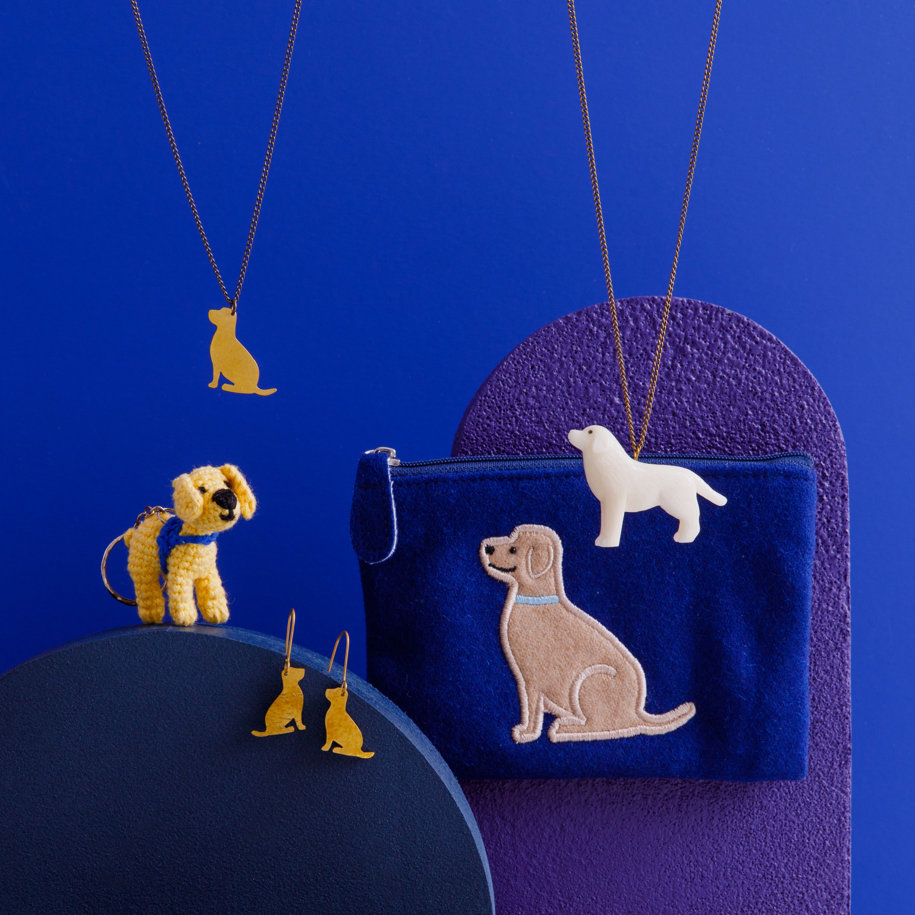 A range of dog shaped jewellery, keyring and purse on a blue background.
