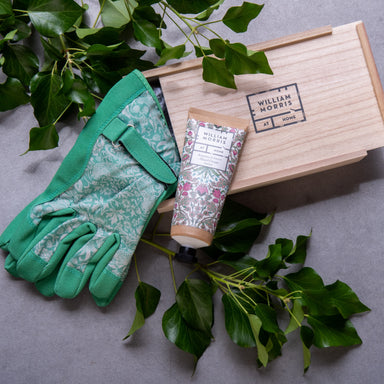 Green floral gardening gloves, hand cream tube and wooden gift box, next to fresh green leaves