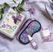 A floral box next to a floral eye mask with velvet ribbon, and spray and sachet of bath salts