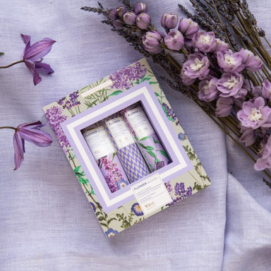 A gift box with 3 hand creams shown, sitting on a lavender material background with dried flowers next to it