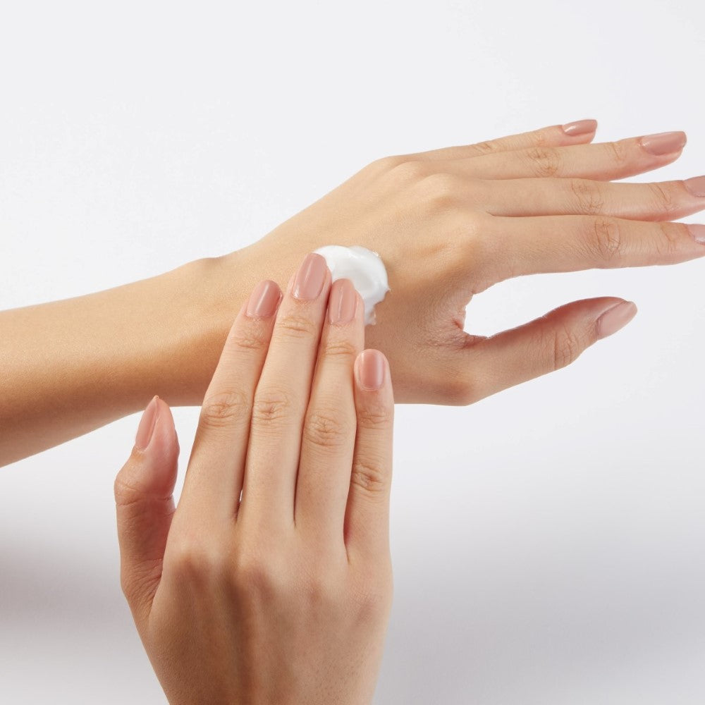 A pair of woman's hands, one hand rubbing cream into the other