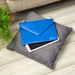 A blue leather envelope resting on top of a tablet and cushion. The envelope has the Guide Dogs logo printed in pale blue on the bottom left corner.