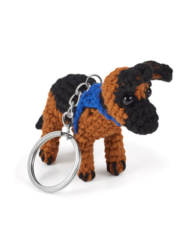 A black and brown crocheted German Shepherd wearing a blue dog coat on a metal keyring.