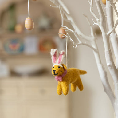 A yellow Labrador felt decoration with pink and white bunny ears and pink bow around neck