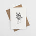 A white greetings card with a black german shepherd design in the middle is above a brown kraft envelope on a white background.