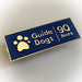 A close up of a Guide Dogs anniversary pin badge. The badge is dark blue with a border and Guide Dogs logo in gold. The badge reads "Guide Dogs 90 Years".