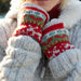 A close up of a lady in a grey knitted coat with her hands close to her face wearing red knitted hand warmers with white reindeers knitted into the pattern.