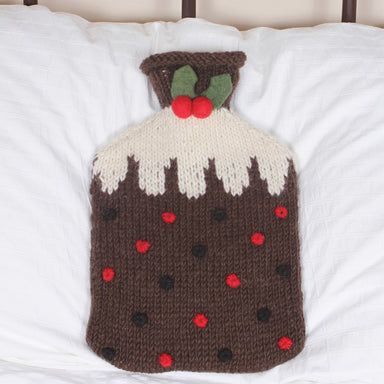 A woollen Christmas pudding hot water bottle lying on a brass bed.