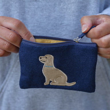 An adult holds a blue felt purse decorated with a Labrador. The inside of the purse is yellow.