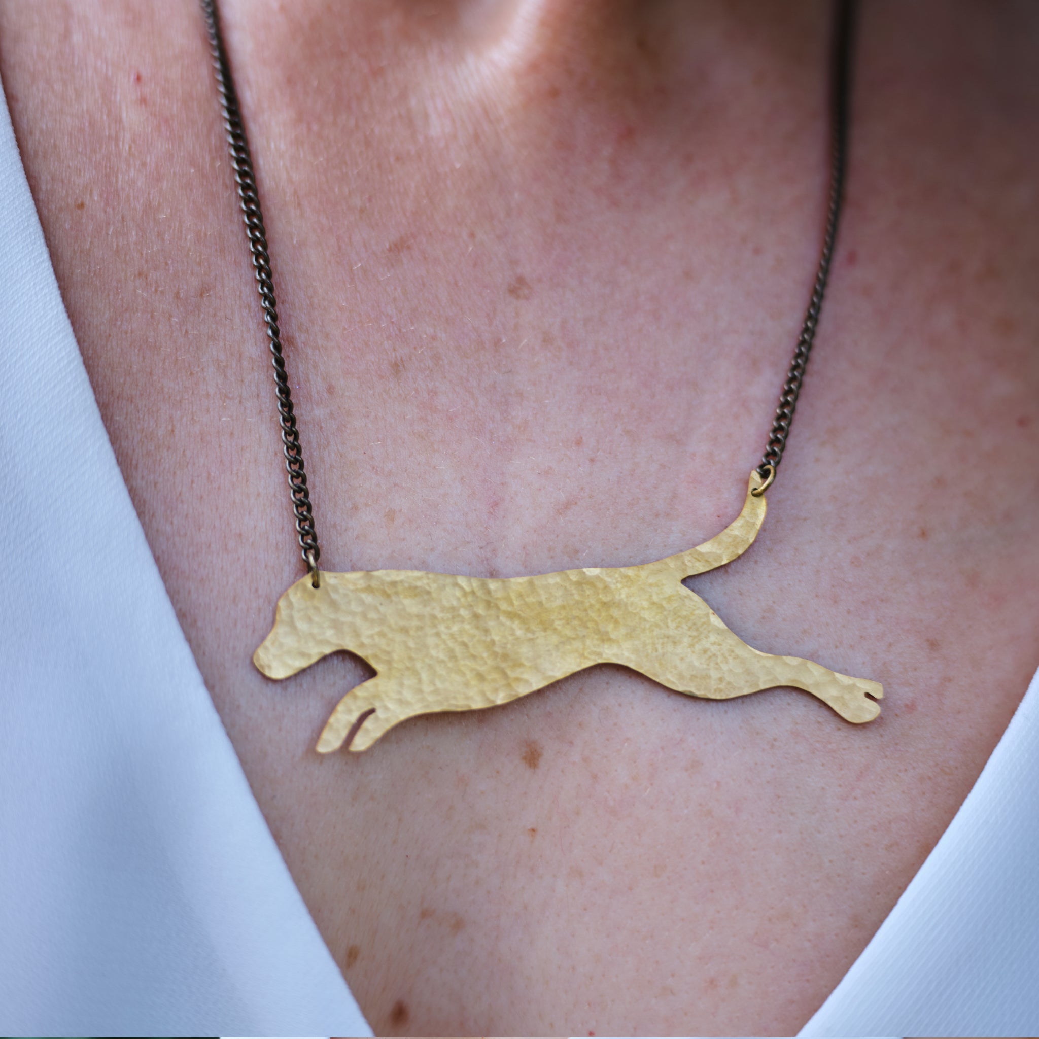 A close up of the leaping dog brass necklace being worn by a lady in a white top.