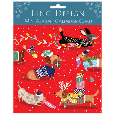The mini advent calendar card decorated with festive dogs wearing jumpers and antlers, carrying presents. There is a dachshund running by, trailing a string of Christmas lights. The background is red with snowflakes. 