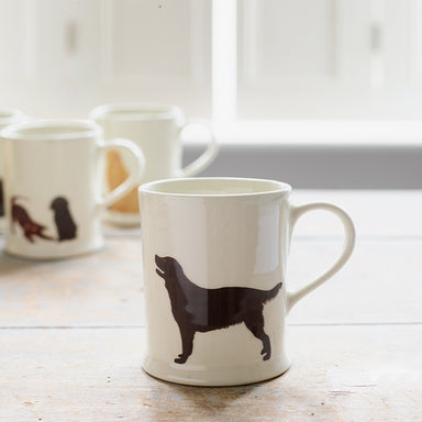 A white ceramic mug with a Black Labrador wagging its tail on a wooden table. 