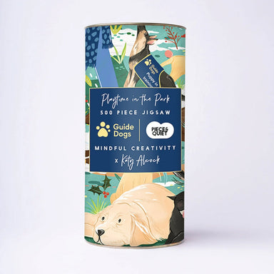 A tube featuring a design with various dogs in a snowy park scene, with a dark blue panel with the text 'Playtime in the Park, 500 piece jigsaw' and the Guide Dogs and Piece & Quiet logos. 