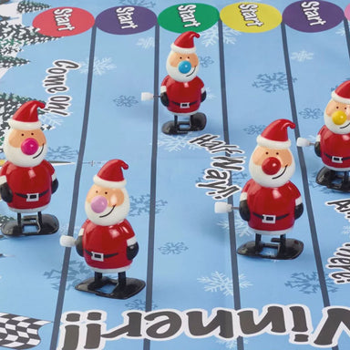 Plastic wind up racing santas are on a blue race track decorated with snowflakes. 