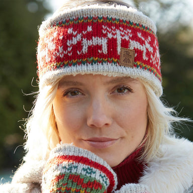 A close up of a lady with blonde hair wearing a red knitted headband with white reindeers knitted into the pattern.