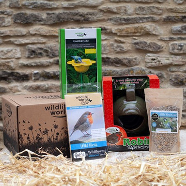 Contents of the For the Love of Gardens Gift pack are out of their box in front of a stone wall. The Petal feeder box is on the gift box, with the wildlife book, the bird seed, and the Robin Teapot Nester arranged in front.